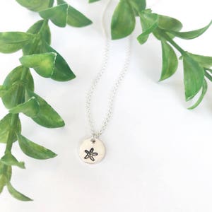 May include: A silver necklace with a small round pendant featuring a simple starfish design.