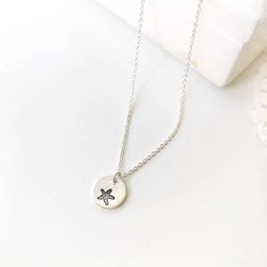 May include: A silver chain necklace with a small round pendant featuring a hand-drawn starfish design.