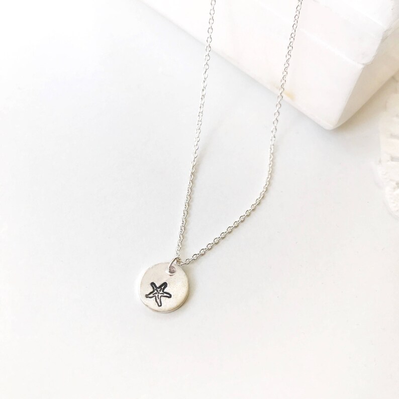 May include: A silver chain necklace with a small round pendant featuring a hand-drawn starfish design.