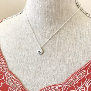 May include: A silver necklace with a small, round pendant featuring a starfish design. The necklace is displayed on a white mannequin with a red and white patterned top.