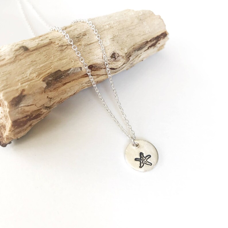 May include: A silver necklace with a small, round pendant featuring a simple, hand-drawn starfish design.