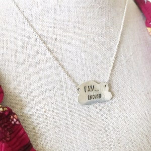 May include: Silver necklace with a cloud-shaped pendant that reads "I AM... ENOUGH".