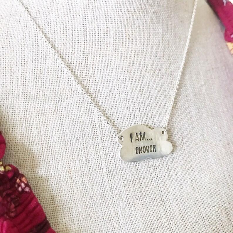 May include: Silver necklace with a cloud-shaped pendant that reads "I AM... ENOUGH".