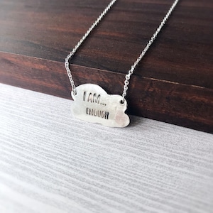 May include: A silver necklace with a cloud-shaped pendant that reads "I AM... ENOUGH".