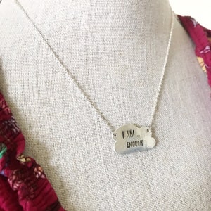 May include: A silver necklace with a cloud-shaped pendant that reads "I AM... ENOUGH".