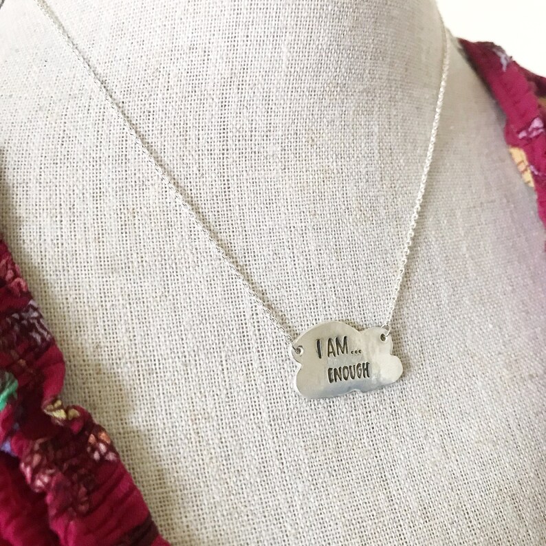 May include: A silver necklace with a cloud-shaped pendant that reads "I AM... ENOUGH".