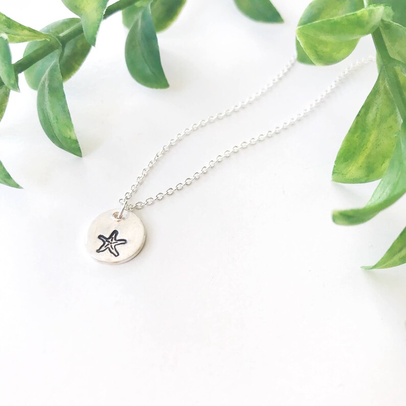 May include: A silver necklace with a small round pendant featuring a stamped starfish design.