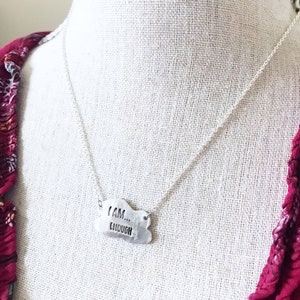 May include: Silver necklace with a cloud-shaped pendant that reads "I AM... ENOUGH".