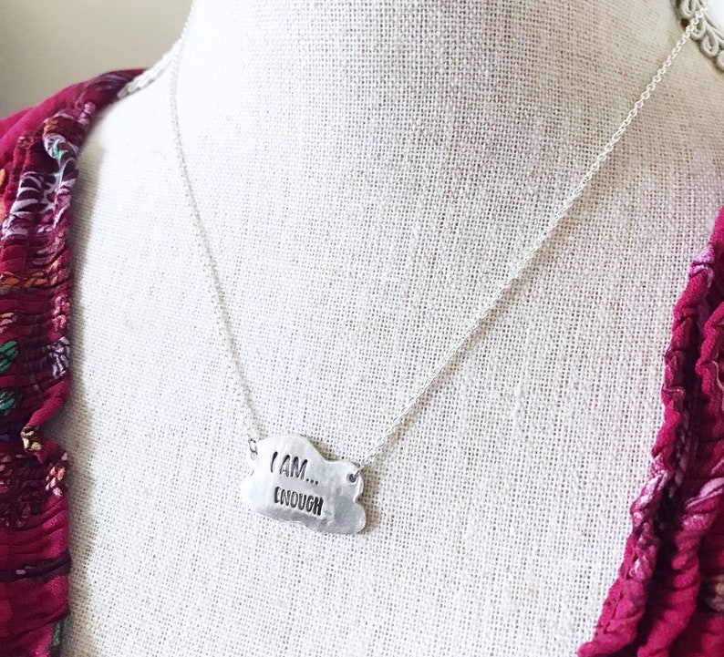 May include: Silver necklace with a cloud-shaped pendant that reads "I AM... ENOUGH".