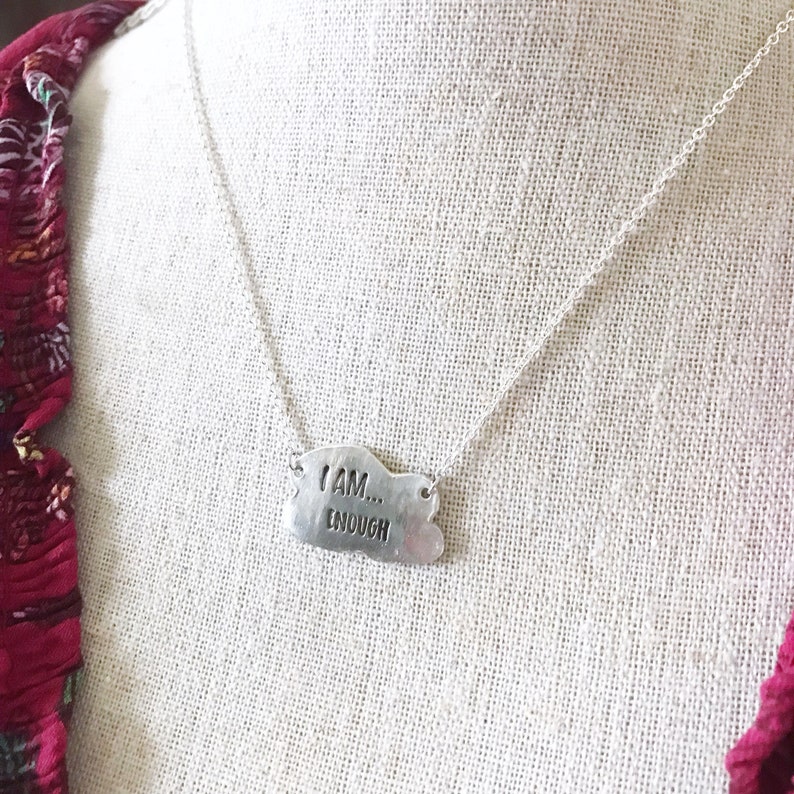 May include: Silver necklace with a cloud-shaped pendant that reads "I AM... ENOUGH".