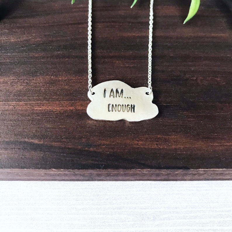 May include: A silver necklace with a cloud-shaped pendant that reads "I AM... ENOUGH".