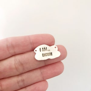 May include: Silver charm in the shape of a cloud with the text "I AM... ENOUGH" engraved on it.