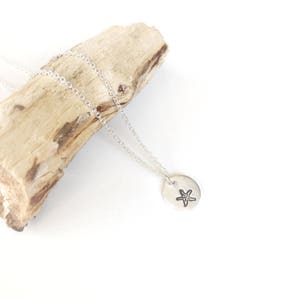 May include: A silver necklace with a delicate chain and a small round pendant featuring a starfish design.