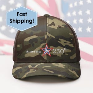 Op de afbeelding: Camouflage baseballpet met een mesh achterkant. De voorkant heeft een rood, wit en blauw sterrenembleem met de woorden "America 250th" in het wit geborduurd. De pet heeft een gebogen klep en een bruine mesh achterkant.