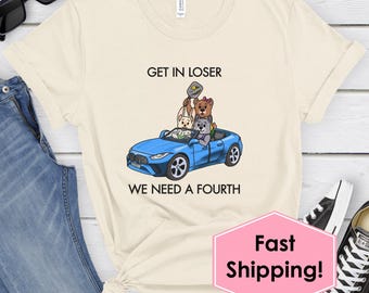 Pode incluir: Camiseta creme com um carro conversível azul e animais de desenho animado. O texto "GET IN LOSER WE NEED A FOURTH" está impresso. A camiseta é combinada com jeans azuis e óculos de sol pretos.