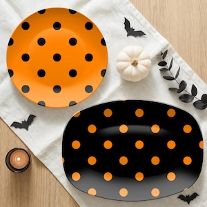 May include: A round orange plate with black polka dots and an oval black plate with orange polka dots. The set features a vibrant color contrast, with the round plate displaying a bright orange surface and the oval plate a deep black surface.