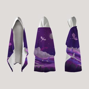 May include: A hooded blanket featuring a fantasy landscape with purple mountains, a starry night sky, and flying dragons. The blanket has a white hood and a soft, plush interior. The design is repeated on the front and back.