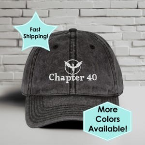 May include: A dark grey baseball cap with a curved peak. The cap has white embroidered text reading "Chapter 40" beneath a bird emblem. The hat has a distressed appearance and a fabric strap closure.