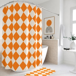 May include: A shower curtain featuring a repeating diamond pattern in vibrant orange and off-white. The curtain hangs from a curved metal rod and is paired with a matching rectangular bath mat on the floor, both displaying the same geometric design.