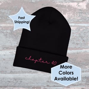 May include: Black beanie hat with the text "chapter 40" embroidered in pink. The hat is folded at the brim and has a classic, casual style. The image also includes text that says "More Colors Available!"