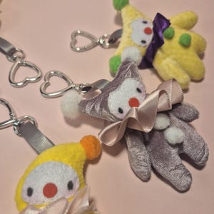 Peut inclure: Gros plan sur plusieurs porte-clés clown en peluche. Les porte-clés présentent une variété de couleurs, notamment le jaune, le violet et le blanc. Chaque clown a un nez rouge et un nœud en ruban. Les porte-clés sont attachés à des fermoirs argentés en forme de cœur.
