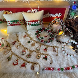 May include: A collection of Christmas-themed jewelry including beaded bracelets with lettered beads spelling Merry Bright, Jesus, and Stank Stunt, gold-tone charm bracelets with holiday icons, and red, white, and green beaded bracelets.
