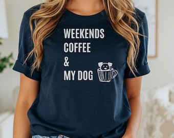 Pode incluir: Camiseta azul marinho com as palavras brancas "WEEKENDS COFFEE & MY DOG". Um gráfico branco de um cachorro em uma xícara de café está ao lado do texto. A camiseta é combinada com shorts jeans azuis.