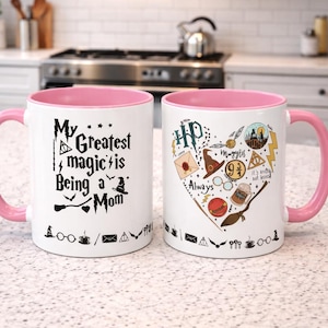 May include: Two white ceramic mugs with pink interiors and handles. One mug features the text "My Greatest magic is Being a Mom" with whimsical illustrations. The other mug has a heart-shaped design with "Always" and "Muggles" text and Harry Potter-themed graphics.