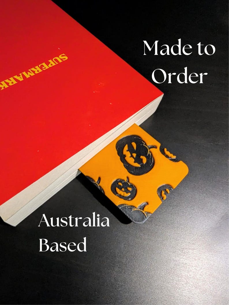 May include: A red book with the word "SUPERMARK" in yellow text. A Halloween-themed bookmark with orange background and black pumpkin faces is inserted into the book. The text "Made to Order" and "Australia Based" are also visible.