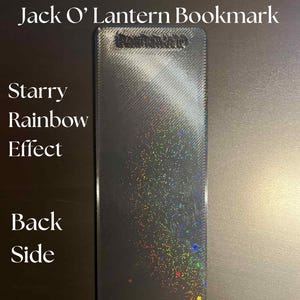 May include: A rectangular bookmark with a starry rainbow effect. The bookmark has a dark gray background with iridescent glitter. The text "Jack O' Lantern Bookmark" is at the top. The words "Starry Rainbow Effect" and "Back Side" are also visible.
