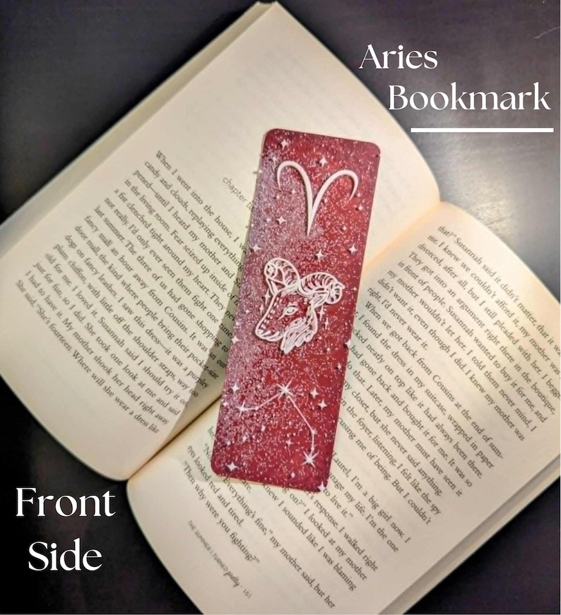 May include: A red Aries bookmark with a white ram illustration and constellation design. The bookmark is rectangular and is shown next to an open book. Text on the bookmark reads "Aries Bookmark".