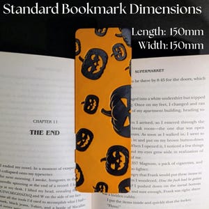 May include: Orange bookmark with black jack-o'-lanterns. The bookmark is rectangular, with dimensions of 150mm in length and 150mm in width. Text on the bookmark reads "Standard Bookmark Dimensions". The bookmark is placed in an open book.