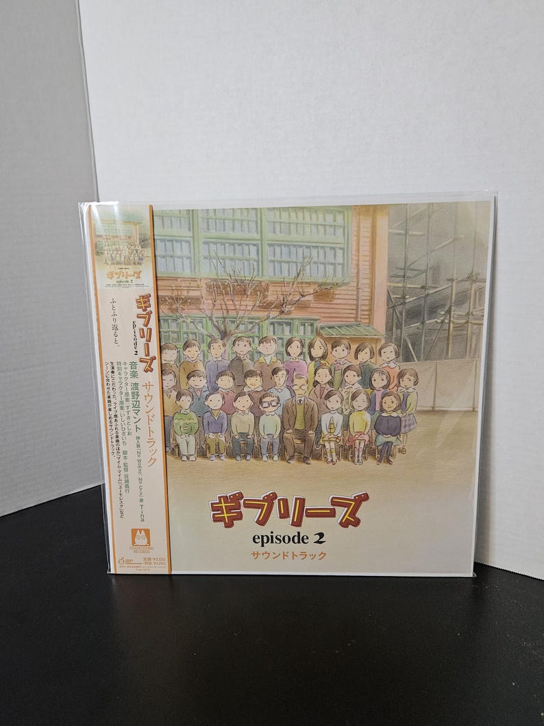 May include: A sealed CD case featuring the artwork for "Ghiblies Episode 2" soundtrack. The cover art depicts a group of people in front of a building. The title is written in Japanese and English. The CD is in a clear plastic sleeve.