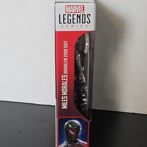 May include: A Marvel Legends Series action figure box featuring Miles Morales in his Brooklyn 2099 suit. The box has a red and white colour scheme with the Marvel Legends logo at the top. The figure is visible through a clear plastic window.