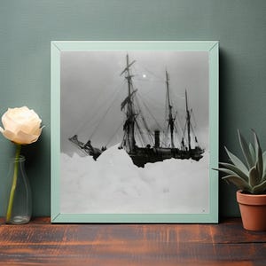 May include: Black and white framed photograph of a tall ship trapped in ice. The ship has multiple masts and rigging, with a dark hull and a light sky in the background. The frame is a light green color.