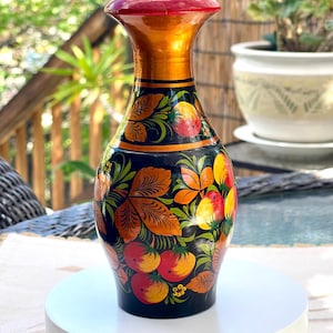 May include: A wooden vase with a black base featuring hand-painted red and yellow fruit motifs, green leaves, and orange accents. The vase has a narrow neck, a flared rim with a solid red top, and a smooth, glossy finish throughout the exterior.