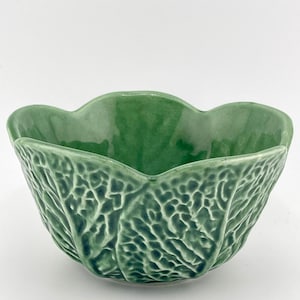 May include: A ceramic bowl with a glossy green finish and a textured exterior that mimics the appearance of overlapping cabbage leaves. The bowl features a scalloped rim and a deep, rounded basin, showcasing a vibrant green color palette.