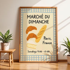 May include: A framed poster with the words "MARCHÉ DU DIMANCHE" and illustrations of croissants, a baguette, and cheese. The poster also says "Paris, France" and "Sundays 9:00 - 13:00". The poster is in a room with plants.