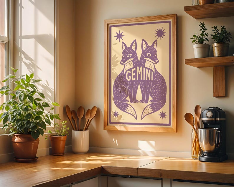 Puede incluir: Una impresi&oacute;n art&iacute;stica enmarcada con dos zorros morados y la palabra "GEMINI". La obra de arte est&aacute; sobre un fondo crema con acentos de estrellas. La impresi&oacute;n se exhibe en un entorno de cocina con estantes de madera y una cafetera.