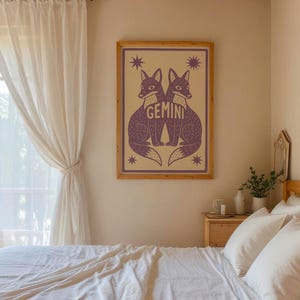 Puede incluir: Un estampado enmarcado con dos zorros morados enfrentados, con la palabra "GEMINI" en el centro. La obra de arte est&aacute; sobre un fondo beige con acentos de estrellas. El estampado se exhibe en una pared de un dormitorio.