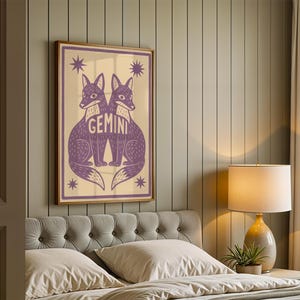 Puede incluir: Un cuadro enmarcado con una ilustraci&oacute;n morada de dos zorros, con la palabra "GEMINI" entre ellos, sobre un fondo crema. La obra de arte enmarcada en madera incluye estrellas. Decoraci&oacute;n de pared.