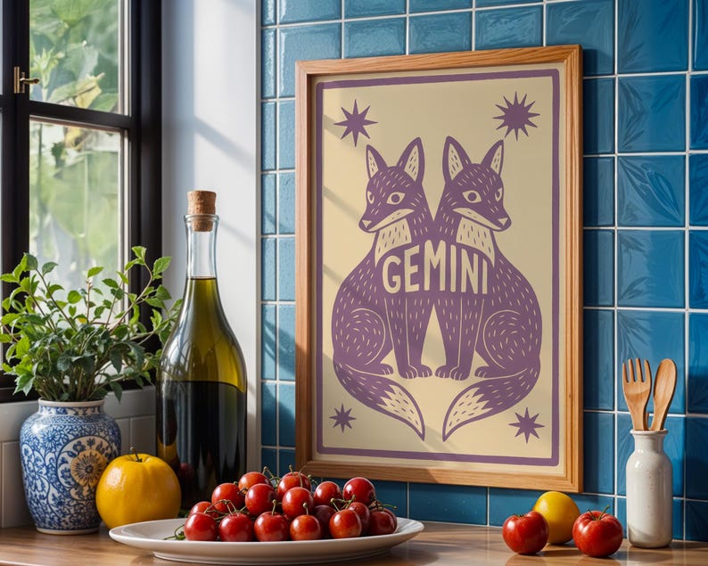 Puede incluir: Un cuadro enmarcado con dos zorros morados y la palabra "GEMINI". La obra tiene un fondo crema con detalles de estrellas, en un marco de madera. Se exhibe en una encimera con una botella de aceite de oliva, un jarr&oacute;n y un plato de tomates.