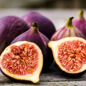 May include: A close-up of several ripe figs, some whole and some halved. The figs are a deep purple color with a creamy interior filled with tiny seeds. The cut figs reveal a vibrant red flesh.