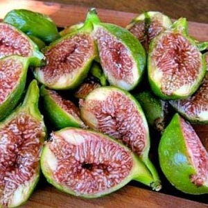 May include: A close-up shot of several fresh figs, some halved to reveal the red and white interior. The figs have green skin and are arranged on a wooden surface. The image highlights the natural colors and textures of the fruit.