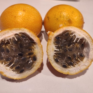 May include: Two whole, round, orange granadilla fruits and two halves, revealing the dark seeds and white pulp. The skin is textured. The fruit is a tropical treat.