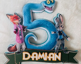 May include: A colorful cake topper featuring characters from Zootopia, including Nick Wilde and Judy Hopps, with a large blue number 5 and the name "Daman" in white letters on a green banner. The topper is designed for a birthday celebration.
