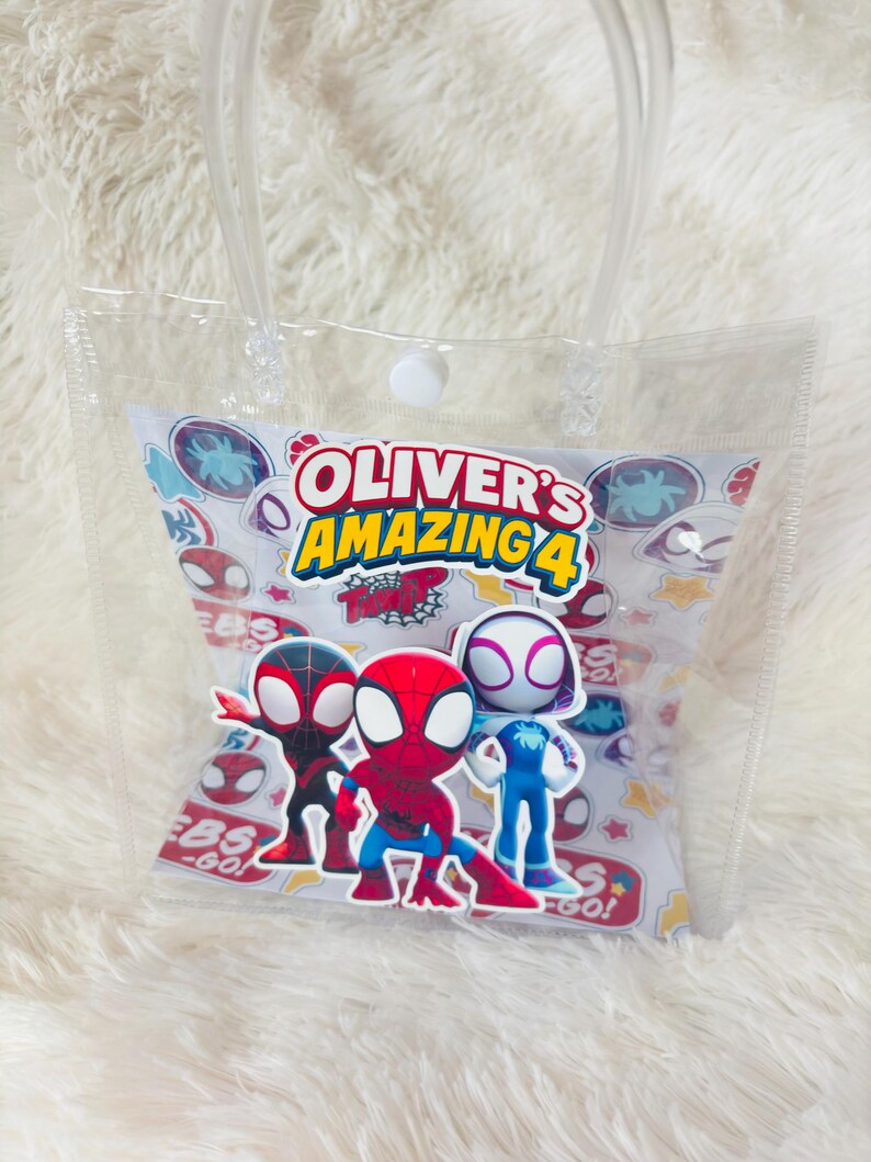 May include: Clear plastic tote bag with a white and patterned insert featuring Spider-Man characters and the text "Oliver's Amazing 4". The bag has a clear handle and a white snap closure.