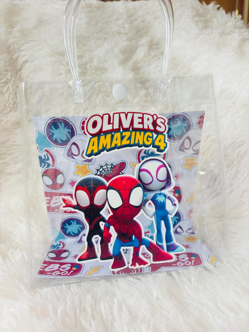 May include: Clear plastic gift bag with transparent handles. The bag features a colorful graphic of Spider-Man characters and the text "OLIVER'S AMAZING 4". The background has a pattern of spider webs and spider symbols.