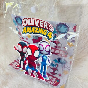 May include: A clear plastic tote bag with a white and colorful insert featuring Spider-Man characters. The insert reads "Oliver's Amazing 4" and includes various Spider-Man logos and graphics. The bag has clear plastic handles.