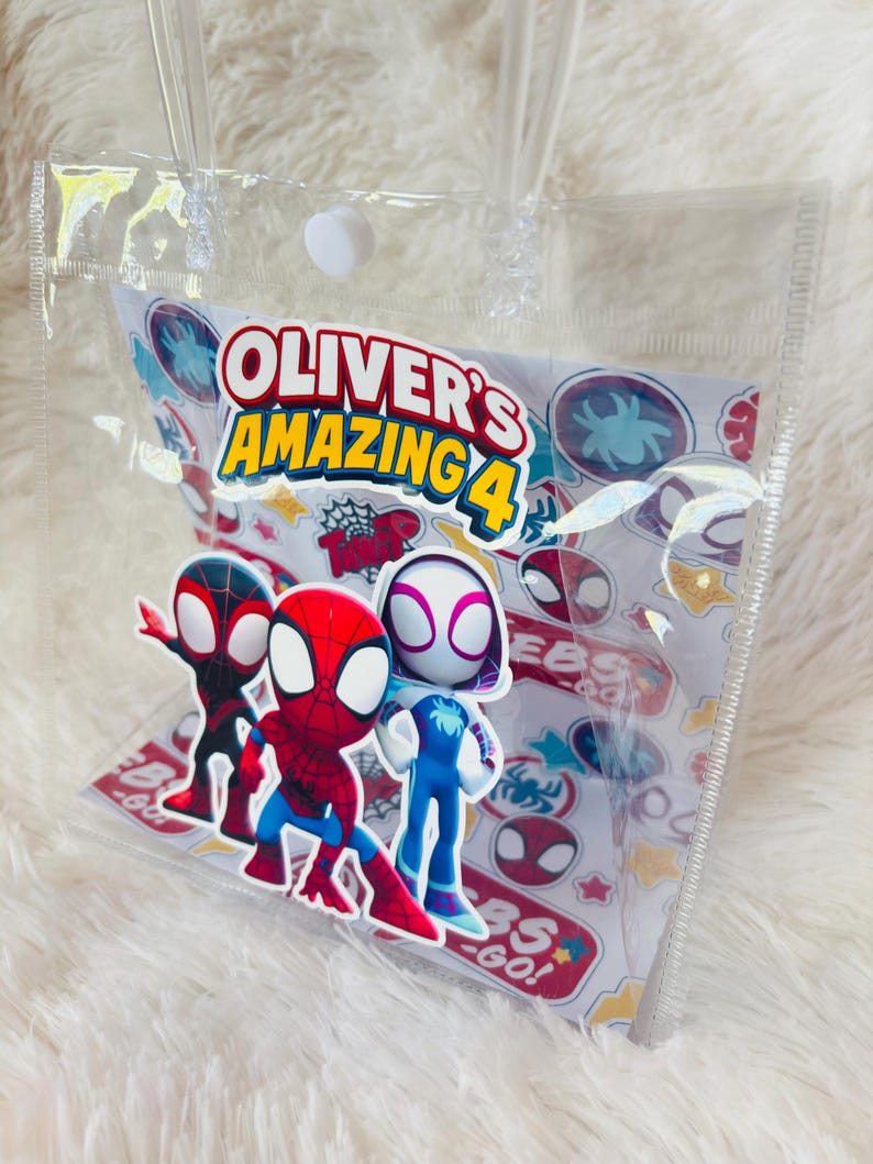May include: A clear plastic tote bag with a white and colorful insert featuring Spider-Man characters. The insert reads "Oliver's Amazing 4" and includes various Spider-Man logos and graphics. The bag has clear plastic handles.